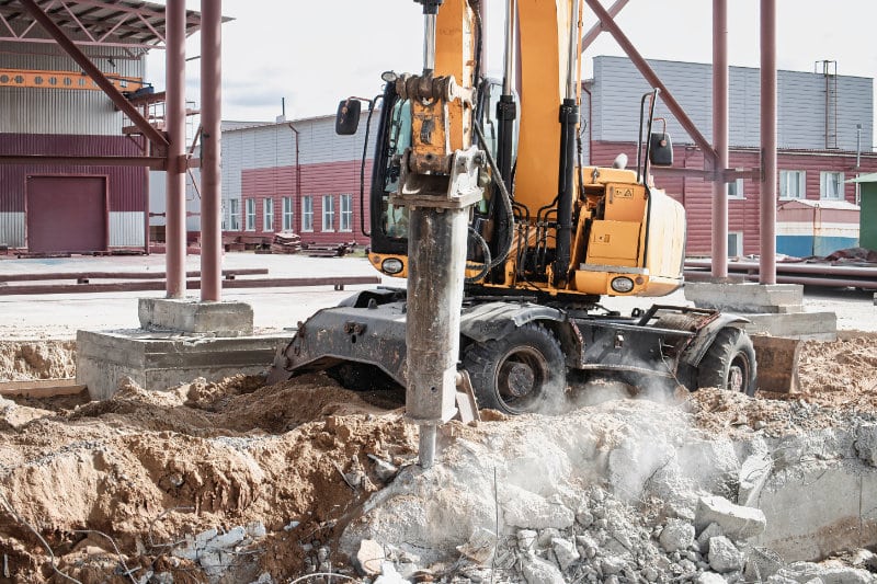 Gibson Design Group Inc. commercial demolition with excavator removing debris and rubble from a building site under clear blue sky.