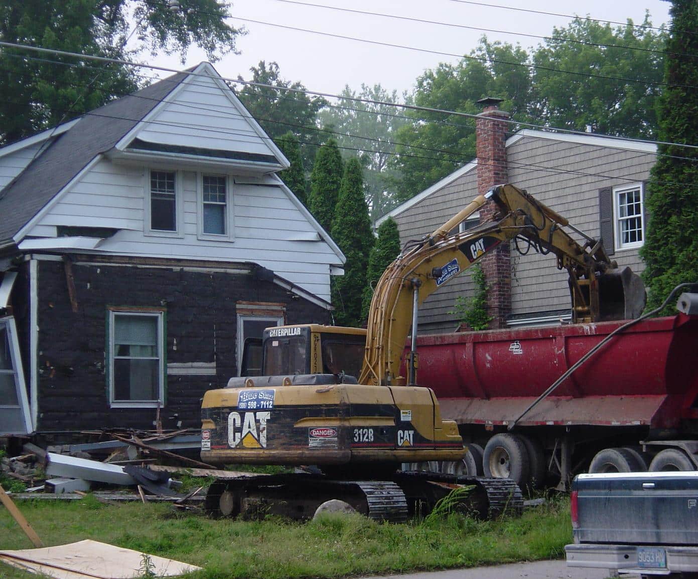 Gibson Design Group Inc. house demolition with heavy equipment excavator tearing down siding into dump truck in Metro Detroit.