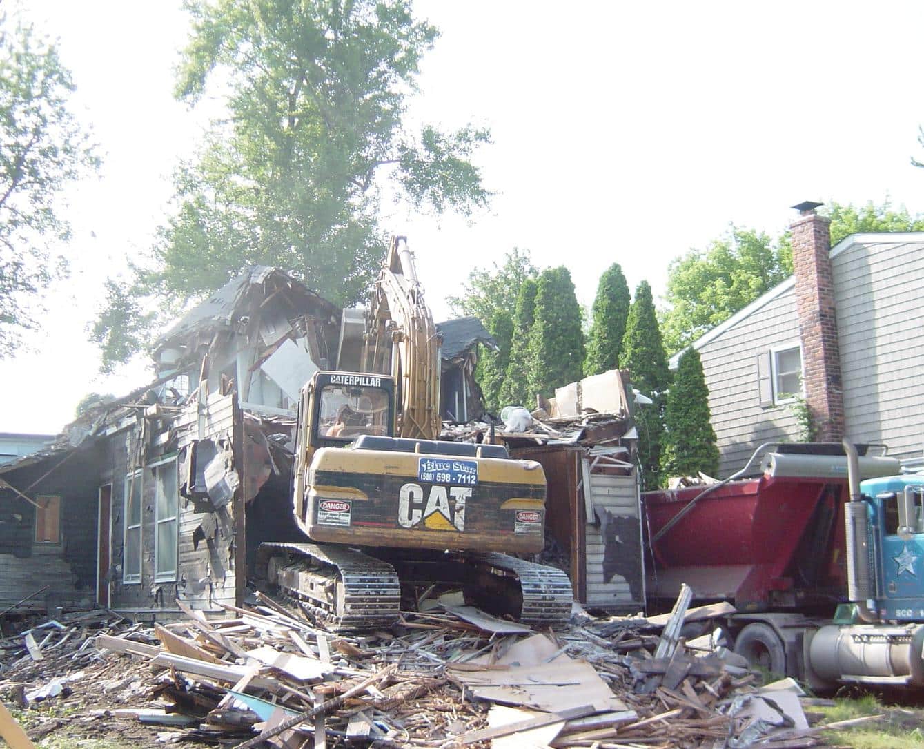 Gibson Design Group Inc. house demolition with excavator tearing down upper story and roof in Metro Detroit.