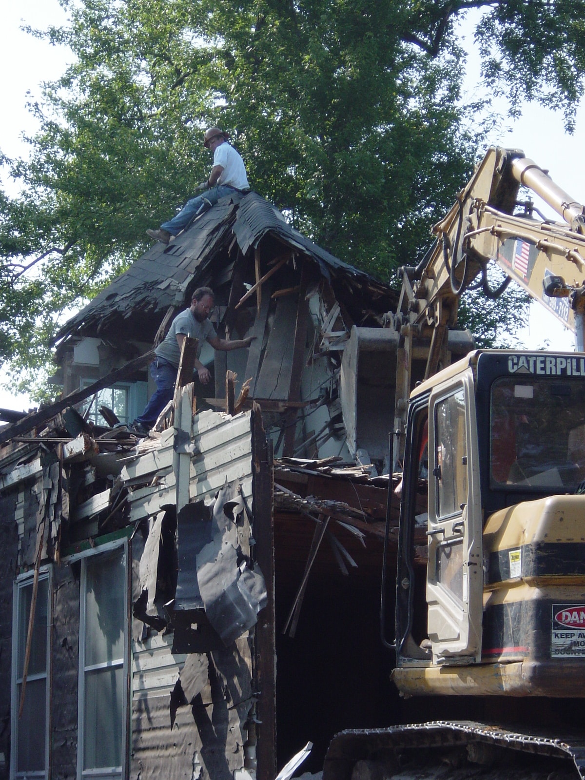 Gibson Design Group Inc. workers manually removing roof shingles during residential demolition in Metro Detroit.